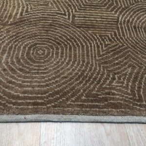 A textured brown rug featuring abstract beige concentric patterns lies on light hardwood flooring.