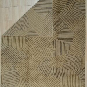 A tan low-pile rug with a dark striped abstract pattern is folded back on light wood flooring.