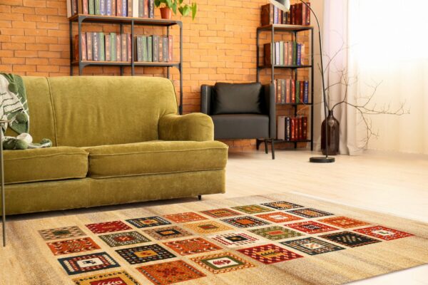 A beige rug patterned with colorful squares anchors a reading nook with a green velvet sofa and brick walls.