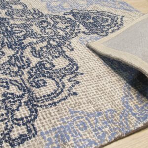 Blue ornamental rug with cream and gray accents, curled back to show the woven reverse on wood planks.