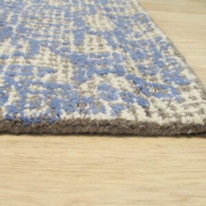 Textured blue, white, and gray rug corner rests on light natural wood flooring.