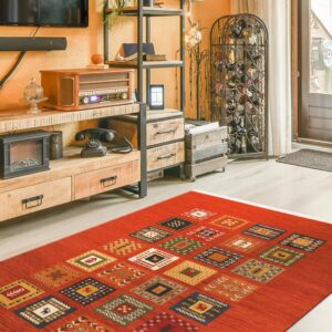 A rust-orange area rug with colorful patterned squares lies on light wood flooring in a cluttered room.
