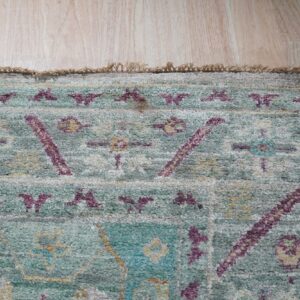 A shaggy rug with distressed teal, cream, and purple geometric patterns rests on light blonde wood planks.