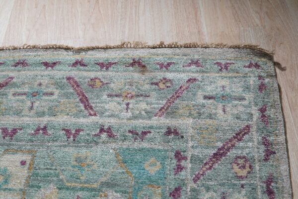 Textured pile rug featuring teal, purple, and gray geometric patterns rests on light wood planks.