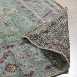 A textured teal, gray, and magenta patterned rug edge is rolled back on light wood flooring.