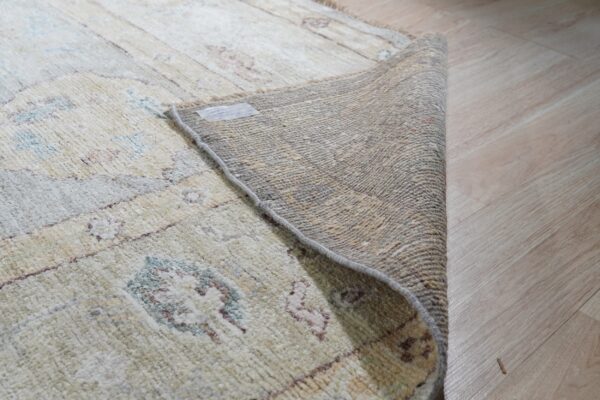 Textured beige rug with subtle patterns is rolled back, revealing its woven backing on a light wood floor.