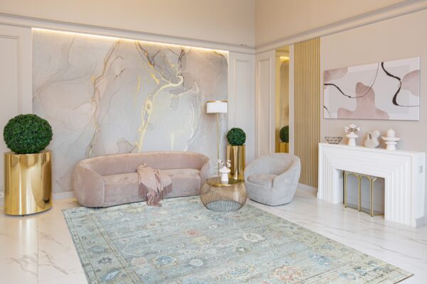 Distressed blue traditional rug on white marble floor beneath a pink velvet sofa and gold accents.