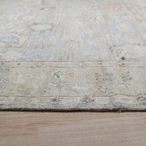 Distressed traditional rug in pale green, blue, and pink colors lies on light wood flooring.