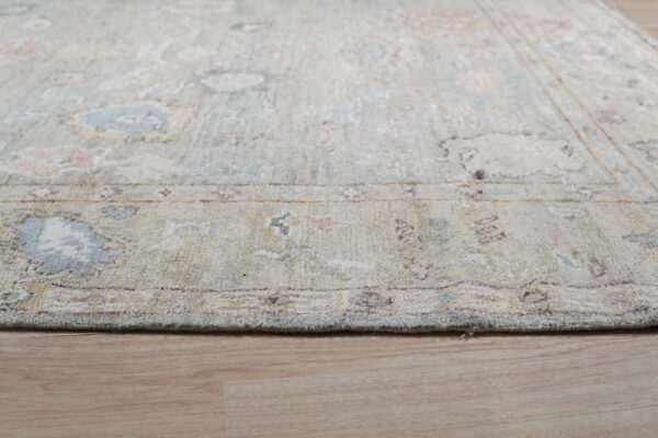 Distressed traditional rug in pale green, blue, and pink colors lies on light wood flooring.