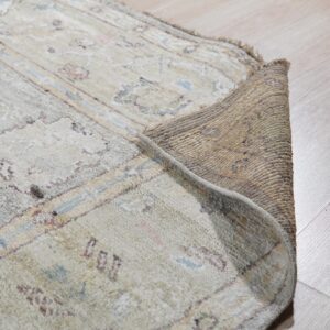 Detail of a rolled-back rug showing the textured backing and soft pale blue and beige pile on wood flooring.