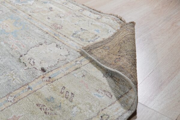 Detail of a rolled-back rug showing the textured backing and soft pale blue and beige pile on wood flooring.