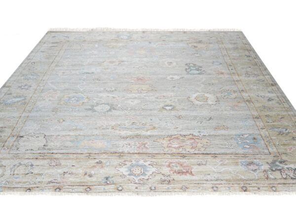 Light gray area rug featuring a distressed floral medallion pattern in pale blue, dusty pink, and yellow.