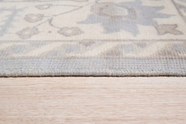 Traditional ivory and light gray floral rug shown in close-up detail on pale wood flooring.