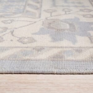 Low-angle view of an ivory, gray, and blue patterned rug edge on light wooden floor.