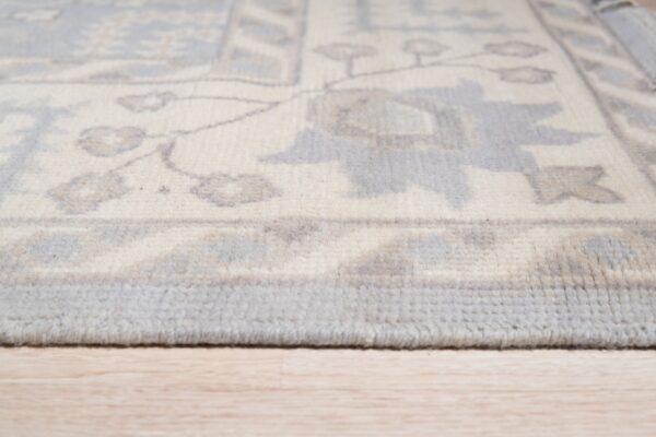 Low-angle view of an ivory, gray, and blue patterned rug edge on light wooden floor.
