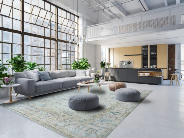 A faded light blue patterned rug anchors a living area in a bright, sunlit industrial loft space.