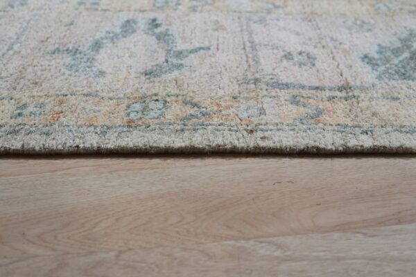 The edge of a textured rug in pale blue, orange, and cream rests on light wood planks.