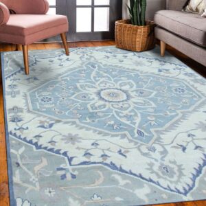 Pale blue traditional medallion rug with cream and dark blue accents in a room with wood floors and chairs.
