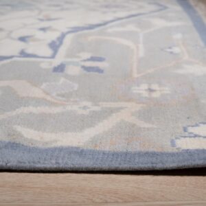 Close-up view of a light blue patterned rug with cream and peach accents resting on wood plank flooring.