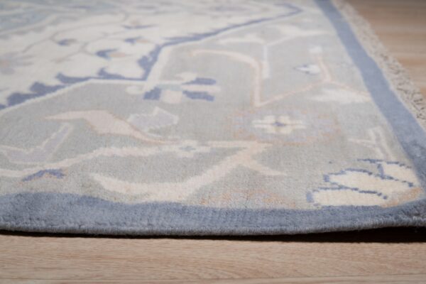Close-up view of a light blue patterned rug with cream and peach accents resting on wood plank flooring.