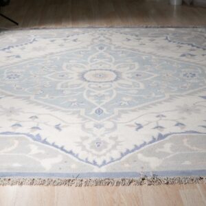 Light blue and cream traditional medallion rug with gray accents lying on light wood plank flooring.