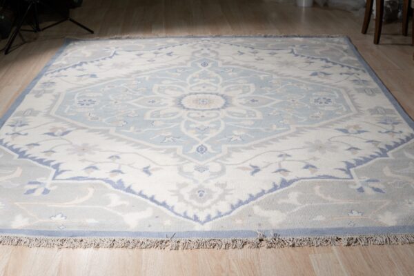 Light blue and cream traditional medallion rug with gray accents lying on light wood plank flooring.