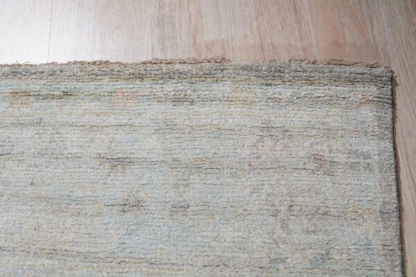 Close-up of a textured, ridged rug in muted cream, gray, and pale blue lying on light wood floor.