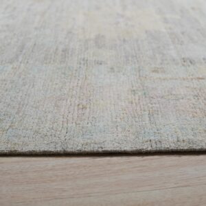 Textured light cream and pastel rug edge shown in close-up over natural blonde wood flooring.