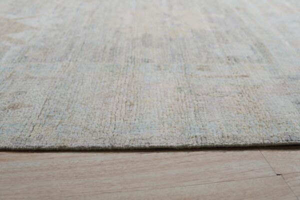 Textured light cream and pastel rug edge shown in close-up over natural blonde wood flooring.