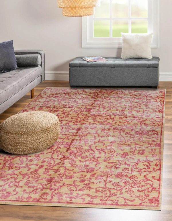Beige rug with pink floral pattern lies on wood floor between a woven pouf and grey ottoman.