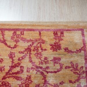 Textured orange rug with a deep pink floral and vine pattern border, placed on light wood floor.