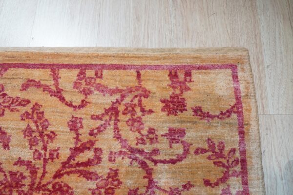 Textured orange rug with a deep pink floral and vine pattern border, placed on light wood floor.
