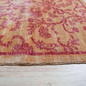 The edge of a gold and deep pink patterned rug rests on pale wood plank flooring.