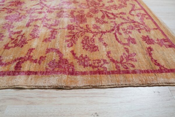 The edge of a gold and deep pink patterned rug rests on pale wood plank flooring.