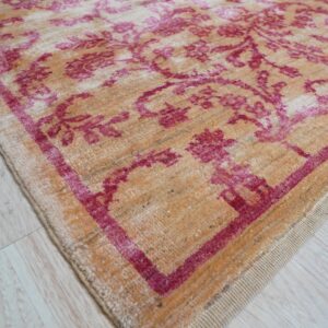 Distressed tan rug with magenta traditional patterns lies on light colored plank flooring.