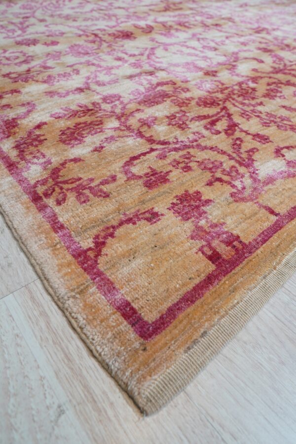 Distressed tan rug with magenta traditional patterns lies on light colored plank flooring.
