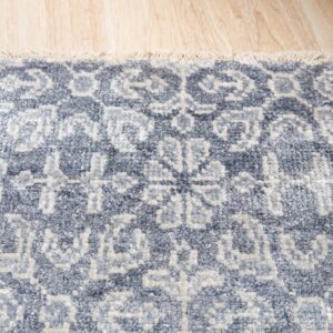 Heavily textured slate blue rug with light geometric patterns and fringe rests on wood flooring.