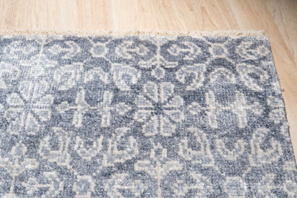 Heavily textured slate blue rug with light geometric patterns and fringe rests on wood flooring.