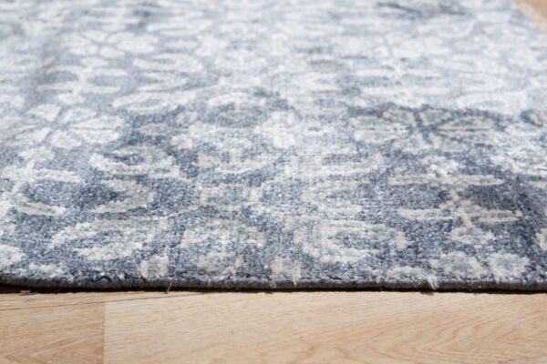 Low-angle view of a textured slate blue and light gray patterned rug lying on light wood planks.