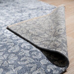 Textured blue and gray patterned rug partially rolled back, showing the woven backing on light wood flooring.