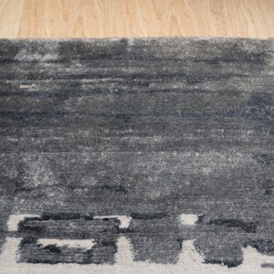 Textured dark gray rug with abstract light gray blocks on a light wood floor.