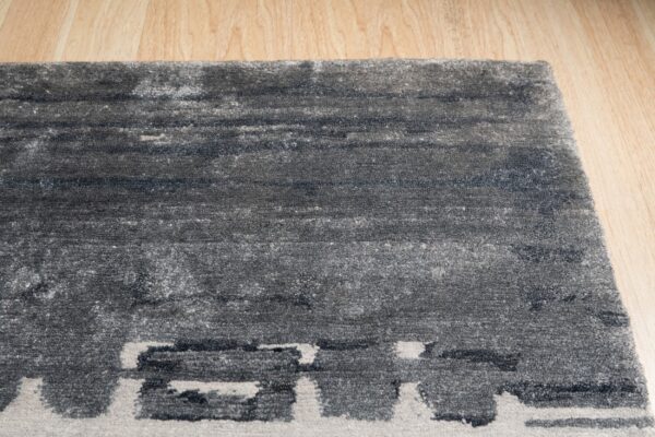 Textured dark gray rug with abstract light gray blocks on a light wood floor.