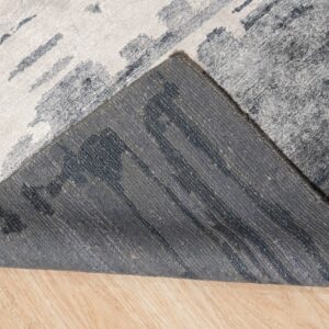 Textured abstract rug in light and dark gray folded on a wood floor, exposing the woven gray backing.