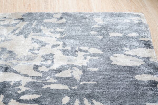 An abstract gray and off-white area rug with contrasting textures rests on light wood planks.