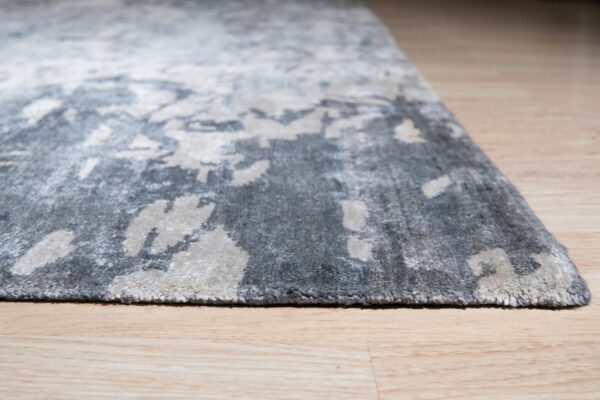 Textured, high-pile gray rug featuring an abstract distressed pattern on light wood plank flooring.