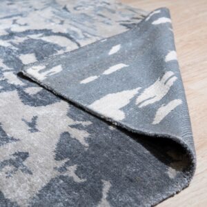 Low pile rug in abstract grey and cream is folded back revealing the woven reverse on wood floor.