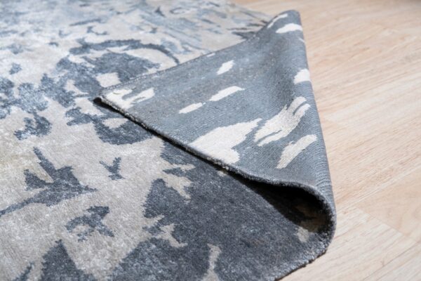 Low pile rug in abstract grey and cream is folded back revealing the woven reverse on wood floor.