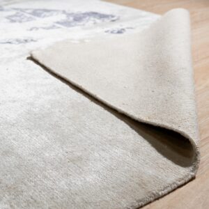 A corner of a cream low-pile patterned rug is folded back on light tan wood flooring.