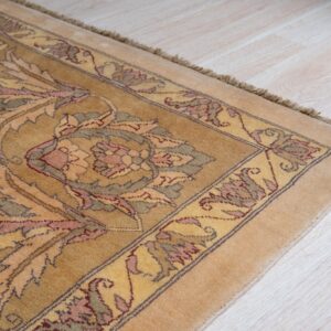 A golden rug displaying intricate pink, green, and yellow floral motifs rests on light wood planks.