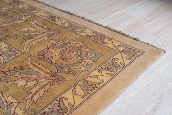 A golden rug displaying intricate pink, green, and yellow floral motifs rests on light wood planks.